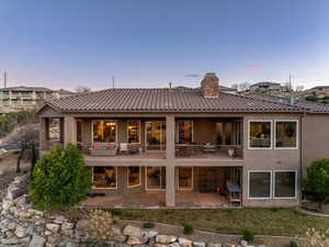 Back of property at dusk featuring a patio area, a tile roof, a chimney, and stucco siding