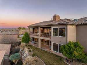 Back of house featuring a patio, a balcony, a tiled roof, stucco siding, and a chimney