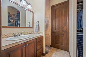 Bathroom featuring decorative backsplash, a walk in closet, vanity, and stone tile floors