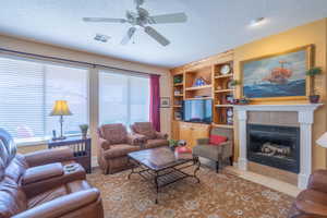 Living area featuring a textured ceiling, a tile fireplace, a ceiling fan, visible vents, and tile patterned floors