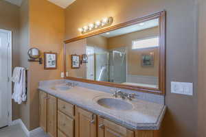 Bathroom featuring double vanity, a shower stall, baseboards, and dual sinks