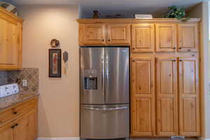 Kitchen featuring knotty alder cabinets, light stone counters, stainless steel fridge, and tasteful backsplash