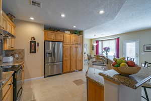 Kitchen featuring stainless steel fridge, visible vents, electric range oven, a kitchen bar, and a sink