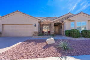 Single story home featuring an attached garage, stone siding, driveway, a tiled roof, and stucco siding