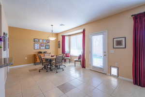 Dining room with bay window, a textured ceiling, baseboards, and light tile patterned flooring