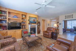 Living room featuring light tile patterned floors, baseboards, a glass covered fireplace, ceiling fan, and built-in entertainment center.