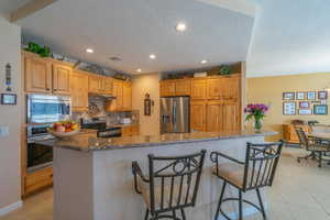 Kitchen with under cabinet range hood, appliances with stainless steel finishes, dark granite countertops, and a center island