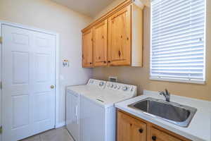 Laundry room with washer and clothes dryer, light tile patterned flooring, a sink, and cabinet space