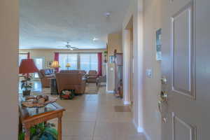 Foyer entrance with light tile patterned floors, ceiling fan, baseboards, and a textured ceiling