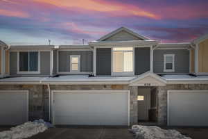 View of property featuring a garage, stone siding, driveway, and board and batten siding