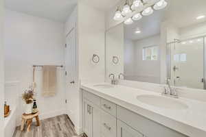 Bathroom featuring double vanity, a stall shower, a sink, and wood finished floors