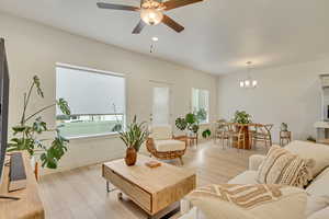 Living area with light wood-style flooring, baseboards, and ceiling fan with notable chandelier