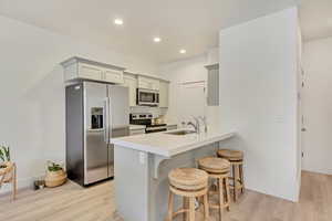 Kitchen featuring a breakfast bar area, appliances with stainless steel finishes, light countertops, gray cabinetry, and a sink