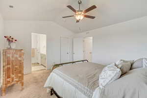 Bedroom with lofted ceiling, light colored carpet, visible vents, and ensuite bath