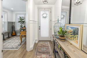 Foyer with light wood-type flooring, wainscoting, a notable chandelier, and a decorative wall