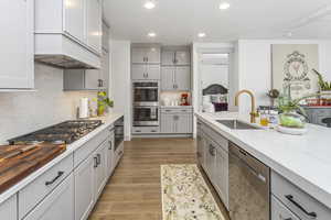 Kitchen featuring appliances with stainless steel finishes, light stone countertops, light wood-type flooring, a sink, and recessed lighting