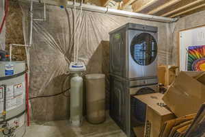 Laundry area featuring strapped water heater, laundry area, and stacked washer / drying machine