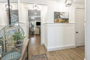 Hallway with a wainscoted wall, a chandelier, a decorative wall, and wood finished floors