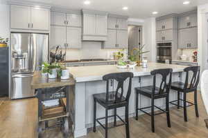 Kitchen with stainless steel appliances, gray cabinets, light countertops, and a kitchen island with sink