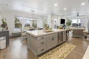 Kitchen with light countertops, stainless steel dishwasher, gray cabinetry, a sink, and an island with sink