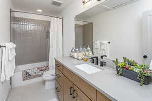 Full bathroom with visible vents, toilet, shower / bath combo with shower curtain, vanity, and tile patterned floors