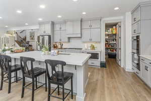 Kitchen featuring a breakfast bar area, light countertops, appliances with stainless steel finishes, gray cabinets, and a center island with sink