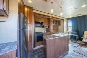 Kitchen with stove, brown cabinets, freestanding refrigerator, hanging light fixtures, and black microwave