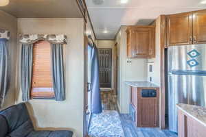 Kitchen with light stone counters, brown cabinetry, wood finished floors, and freestanding refrigerator