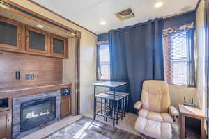 Living area featuring light wood-style floors, a wealth of natural light, a glass covered fireplace, and crown molding