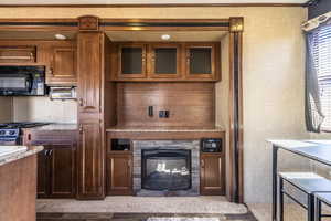 Kitchen with black appliances, light stone counters, a glass covered fireplace, and glass insert cabinets