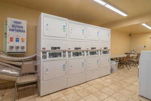 Community laundry room with light tile patterned flooring and stacked washer and clothes dryer