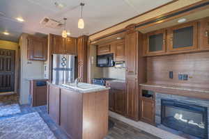 Kitchen with an island with sink, glass insert cabinets, decorative light fixtures, stainless steel appliances, and a sink