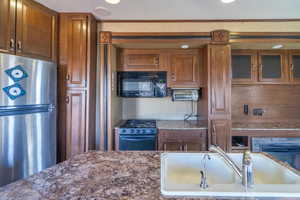 Kitchen featuring stove, glass insert cabinets, freestanding refrigerator, a sink, and black microwave