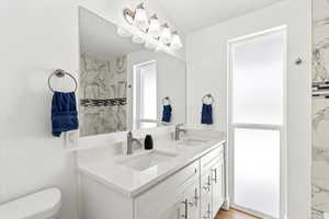 Full bath featuring toilet, a double sink vanity, and floor to ceiling window.