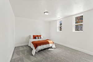 Bedroom with light colored carpet, a textured ceiling, and windows.