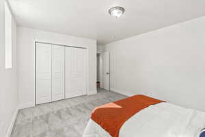 Bedroom featuring a textured ceiling, a closet, and light colored carpet.