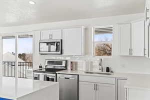 Kitchen with a sink, stainless steel appliances, quartz countertops, white cabinetry, and sliding door.