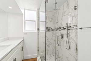 Bathroom featuring a marble finish shower, euro glass surround, wood finished floors, and quartz counter vanity.