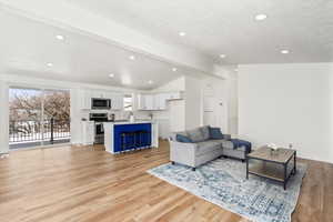 Living area, kitchen, and dining room featuring vaulted ceiling with beams, light wood finished floors, and recessed lighting