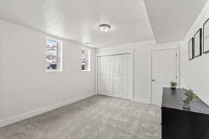 Bedroom with light colored carpet, closets, a textured ceiling, and windows.