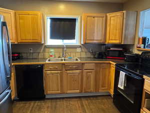 Kitchen featuring dark wood-style floors, black appliances, a sink, and tile countertops