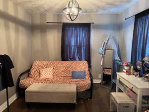 Living area featuring dark wood-style floors, a chandelier, a textured ceiling, and baseboards