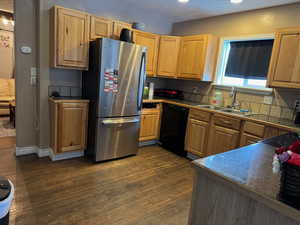 Kitchen with black dishwasher, dark wood-style flooring, freestanding refrigerator, a textured ceiling, and a sink