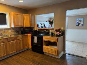 Kitchen with wainscoting, dark wood-style flooring, a textured ceiling, black range with electric cooktop, and a sink