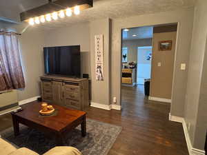 Living room with dark wood-style flooring, a textured ceiling, baseboards, and heating unit