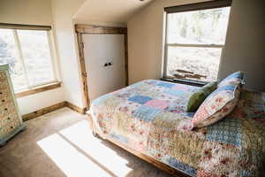 Carpeted bedroom with a closet, multiple windows, vaulted ceiling, and baseboards