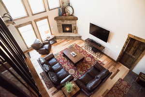 Living room with a stone fireplace, wood finished floors, a high ceiling, and baseboards