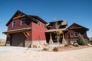 View of front of house with an attached garage, stone siding, concrete driveway, roof with shingles, and board and batten siding