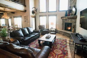 Living room with a chandelier, wood finished floors, a wealth of natural light, and a stone fireplace