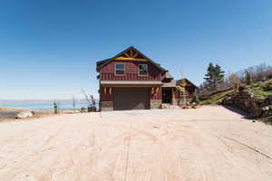 View of front of property with a water view, board and batten siding, a garage, stone siding, and driveway
